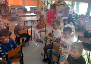 Dzieci siedzą na krzeskach udając jazdę na koniach.