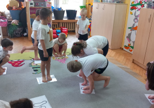 Przedszkolaki stoją na kartkach z narysowanymi stopami.