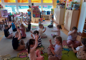 Przedszkolaki siedzą w parach naprzeciw siebie z uniesionymi patyczkami.