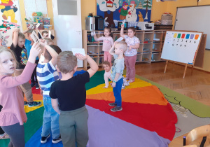 „Krasnoludki” stoją na chuście animacyjnej, unoszą kartoniki z cyframi.