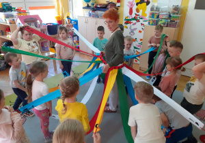 Krasnoludki stoją dookoła p. Agnieszki trzymając szarfy naprzemiennie wysoko lub nisko.