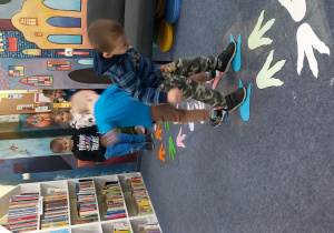 Przedszkolaki chodzą po śladach łap dinozaura.