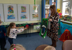 Oliwka celuje woreczkiem do paszczy dinozaura.