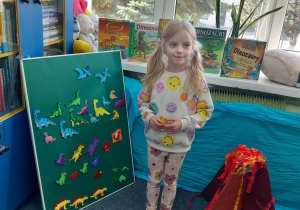 Kaja pozuje do zdjęcia na tle książek z dinozaurami.