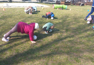 Przedszkolaki dotykają piłkę czołem głowy.
