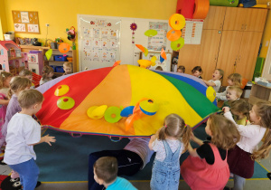 Dzieci machają chustą animacyjną, aby wyleciały wszystkie krążki-owoce.