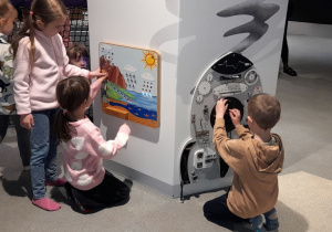 Emilka, Oliwia, Ada i Łucja bawiąc się kolorową planszą poznają podstawowe zjawiska przyrodnicze, a Jasiu manipuluje mechanizmem z pokrętłami i kołami zębatymi.