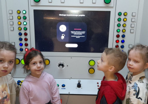 Dzieci stoją przy interaktywnym panelu, dzięki któremu mogą sterować statkiem kosmicznym, wcielając się w rolę astronautów.