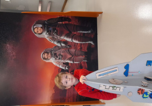 Antoś, Łucja i Ada bawią się przy interaktywnej rakiecie i pozują do zdjęcia jako mali astronauci.