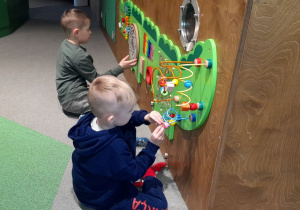 Jakub i Franek bawią się przy tablicach manipulacyjnych, rozwijając sprawność manualną.