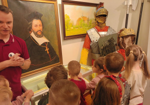 Kustosz muzeum rozmawia ze zwiedzającymi na temat kolejnych eksponatów przedstawiających strój Łaskich Rzymian oraz obrazów Kolegiaty i Jana Łaskiego.