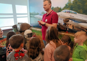 W sali poświęconej lotnictwu przedszkolaki oglądają stare wyposażenie pilotów.