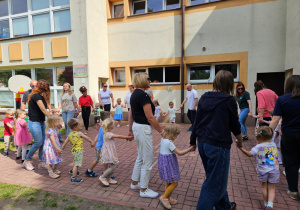 Panie wraz z dziećmi, rodzicami i dziadkami obracają się w kole podczas zabawy "Kółko graniaste"