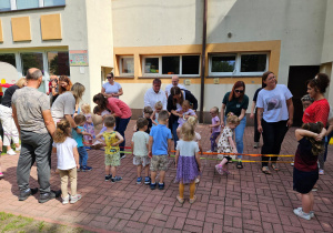 Chętne osoby przeskakują przez gumę, którą trzyma na kolanach pani Kamilka i pani Ania