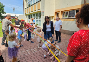 Dzieci przechodzą pod gumą, którą trzyma na kolanach pani Kamilka i pani Ania