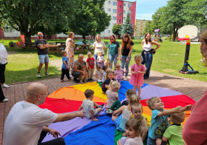 Dzieci wraz z rodzicami siadają na kolorze zielonym chusty animacyjnej