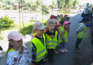 Dzieci stoją skupione na opowieściach pani przewodnik i obserwują zwierzęta przed nimi