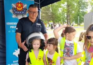 Łucja ma okazję przymierzyć policyjny kask z przyłbicą podczas prezentacji wyposażenia funkcjonariuszy.