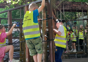 Grupa przedszkolaków zwinnie pokonuje drewniany tor przeszkód, ćwicząc sprawność i świetnie się przy tym bawiąc.
