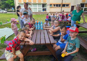 Dzieci z grupy "Żabek" siedzą przy stoliku na placu zabaw