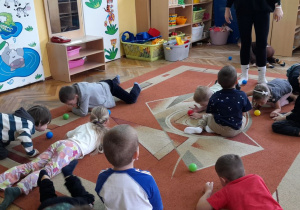 Przedszkolaki za pomocą oddechu przemieszczają piłeczkę po dywanie.