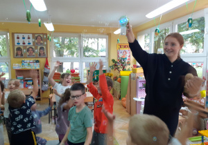 Pani instruktor puszcza bańki, które dzieci łapią w powietrzu.