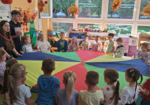 Wszyscy trzymają kolorową chustę animacyjną i słuchają poleceń pani Agaty.