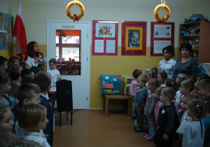 Odśpiewanie hymnu Polski przez przedszkolaki i wychowawczynie w kąciku naszego patrona.