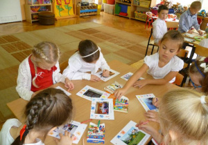 Dzieci przy stoliku ozdabiają kartki ze zdjęciami;