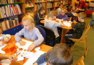 Przedszkolaki siedzą przy stolikach i naklejają białe i czerwone serduszka w formie flagi.