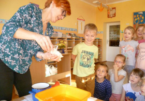 Wychowawczyni nalewa z garnuszka wosk do miski z wodą, przed nią stoi Emil i kilkoro dzieci.