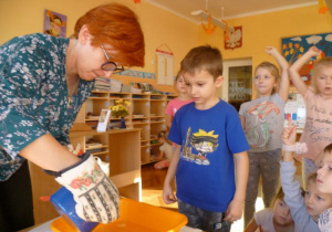  Nauczycielka pokazuje Olkowi i grupie dzieci otrzymaną figurę z przelanego wosku.