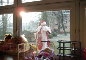 Mikołaj zagląda przez okno w przedszkolu, czy to w tym przedszkolu na niego czekają dzieci.