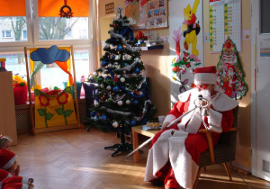Mikołaj odpoczywa w fotelu po dalekiej i długiej drodze i rozmawia z dziećmi.