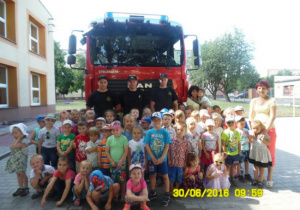 Dzieci ze strażakami a tle strażacki samochód bojowy