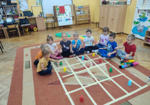 Dzieci na dywanie układają kubeczki według określonego kodu, na stworzonej macie do kodowania.