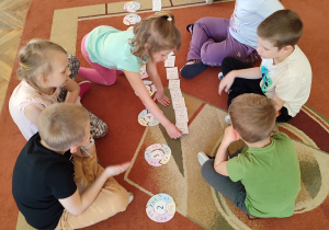 Dzieci na dywanie grają w "Matematyczne puzzle" i "Matematyczne ja mam kto ma?".