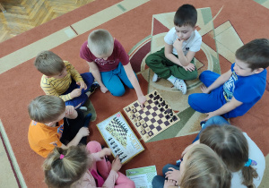 Dzieci siedzą na dywanie wspólnie grają w szachy.