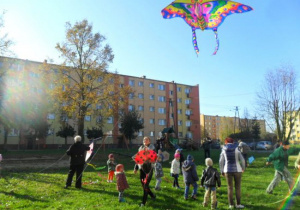 Dzieci wspólnie z rodzicami w ogrodzie przedszkolnym puszczają latawce
