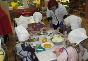 Pani dyrektor pomaga dzieciom, które robią sałatkę warzywno-owocową.