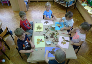 Siedzący przy stoliku: Blanka, Mateusz T., Franek, Oliwier, Kamil M. i Amelka tworzą zwierzęta z liści.