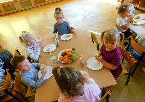 Dzieci jedzą i piją siedząc przy stoliku.