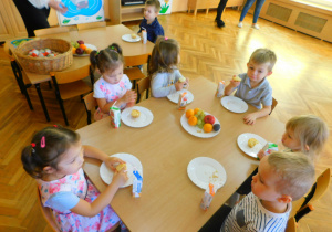 Dzieci jedzą i piją siedząc przy stoliku.