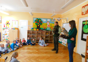 Dzieci ze ‘Słoneczek’ słuchają ciekawostek o sowie i sokole, które opowiada pan leśniczy.