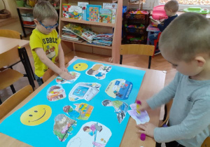 Maluchy przyglądają się ilustracjom przedstawiającym różne formy zabawy, a następnie naklejają na kartkę.