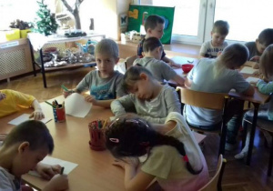 Dzieci siedzą na dywanie i pokazują wykonane rysunki filmującemu licealiście;