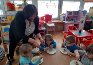 Pani Halinka pokazuje dzieciom jak należy nabierać makaron na widelec przy użyciu łyżki.