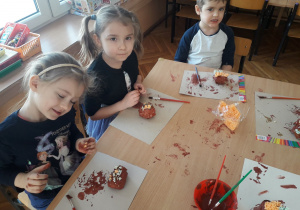 Natalka, Ligia i Antek ozdabiają pomalowane „pączki” kolorową posypką ze styropianu.