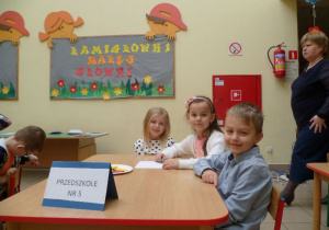 Olek, Nikola i Zosia siedzą przy stoliku z podpisem Przedszkole Nr 5;