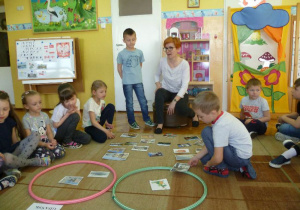  Dzieci na dywanie segregują zdjęcia miast do dwóch obręczy, Olek wybiera jedno z nich;